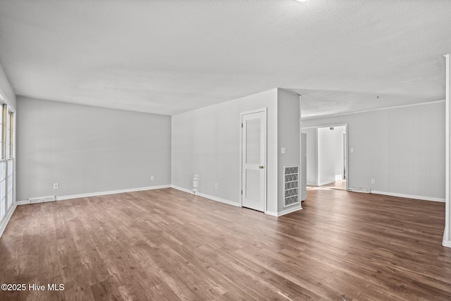 empty room with wood finished floors, visible vents, and baseboards