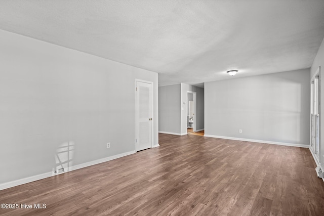 empty room featuring a textured ceiling, baseboards, and wood finished floors