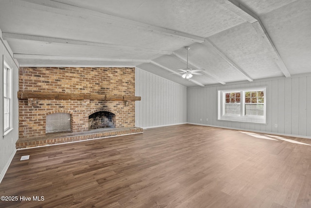 unfurnished living room featuring baseboards, lofted ceiling with beams, ceiling fan, wood finished floors, and a fireplace