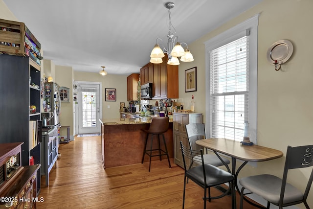 kitchen featuring stainless steel microwave, brown cabinets, a peninsula, light wood-style floors, and a notable chandelier