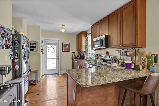 kitchen featuring brown cabinetry, a peninsula, a sink, appliances with stainless steel finishes, and light wood-type flooring