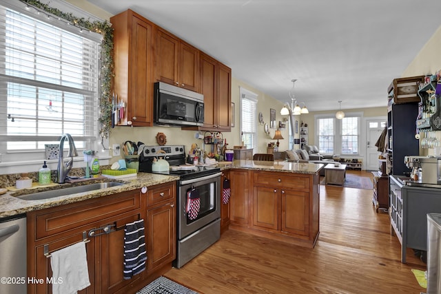 kitchen featuring brown cabinetry, light wood finished floors, a peninsula, a sink, and stainless steel appliances