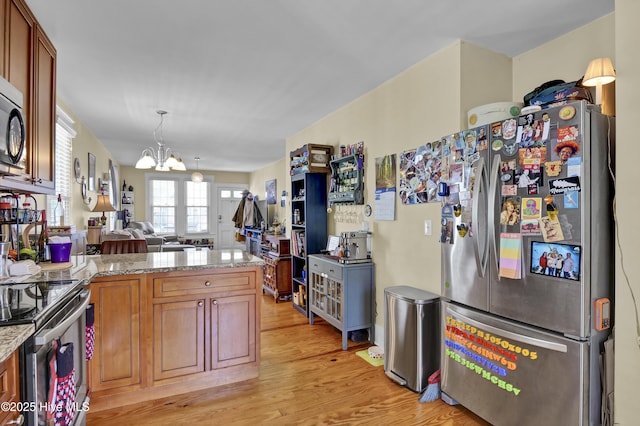 kitchen with light wood-style flooring, open floor plan, a peninsula, appliances with stainless steel finishes, and a chandelier