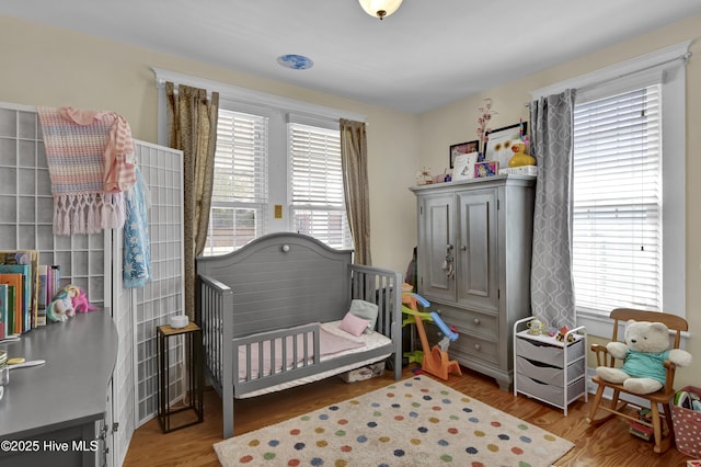 bedroom featuring multiple windows, a nursery area, and wood finished floors