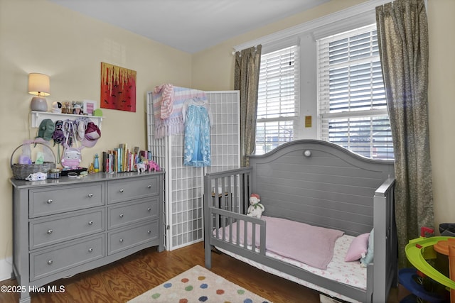 bedroom featuring a nursery area and dark wood-style floors