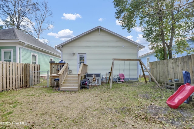 back of property featuring a deck, a playground, a fenced backyard, and a lawn