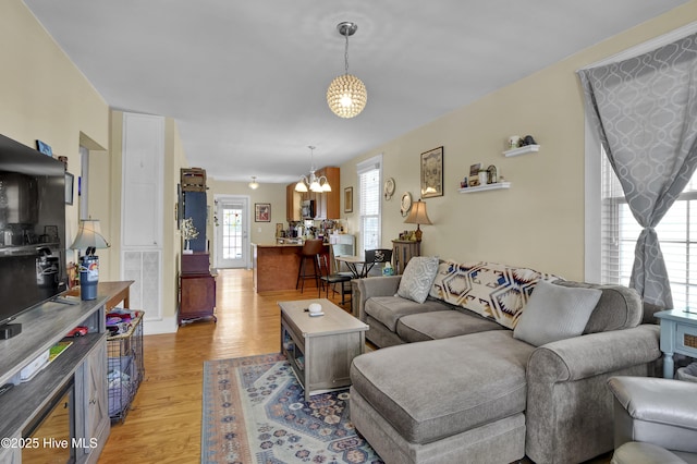 living area featuring visible vents, light wood-style floors, and an inviting chandelier