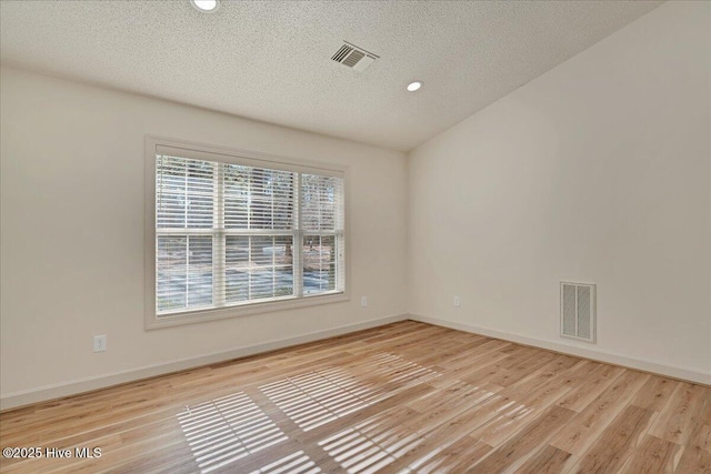 empty room featuring light wood finished floors, baseboards, visible vents, and a textured ceiling