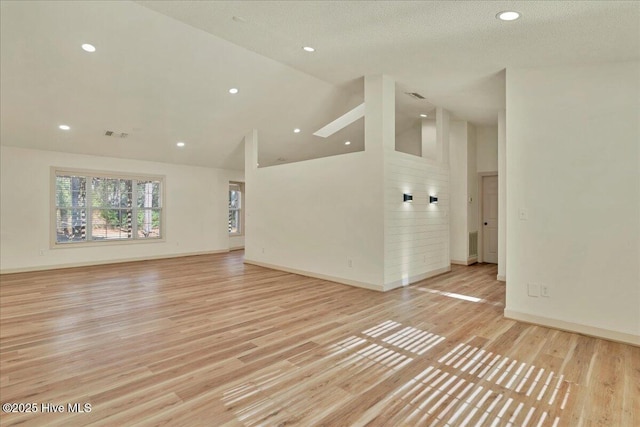 empty room featuring light wood-style floors, high vaulted ceiling, and baseboards