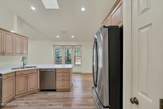 kitchen featuring a skylight, appliances with stainless steel finishes, light brown cabinets, a sink, and a peninsula