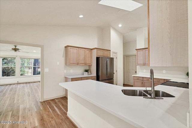 kitchen featuring light wood finished floors, light countertops, light brown cabinetry, freestanding refrigerator, and a sink