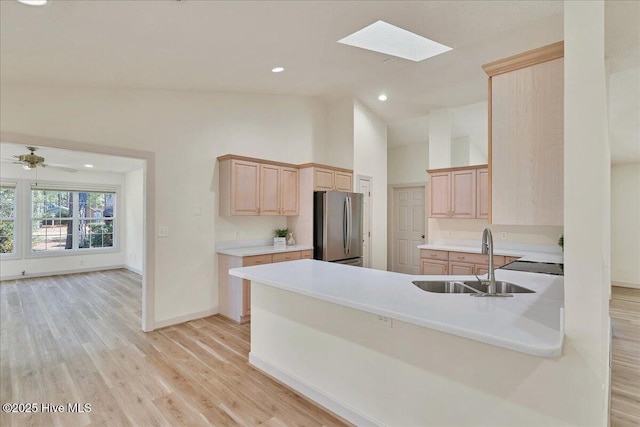 kitchen featuring light countertops, light wood-style flooring, freestanding refrigerator, light brown cabinets, and a sink