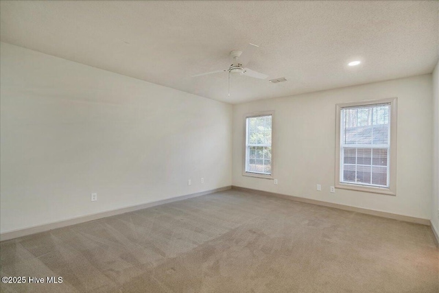 spare room with visible vents, baseboards, a ceiling fan, light colored carpet, and a textured ceiling