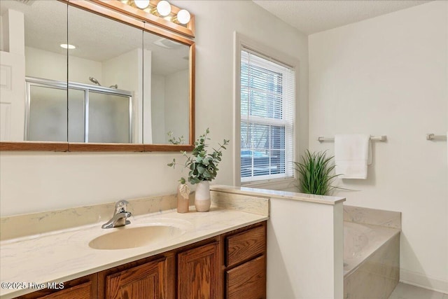 full bathroom featuring a textured ceiling, a stall shower, a garden tub, and vanity