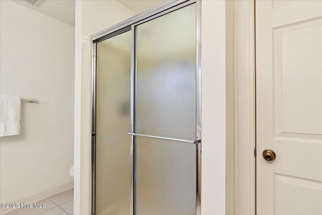 full bath featuring baseboards, toilet, tile patterned floors, a textured ceiling, and a shower stall