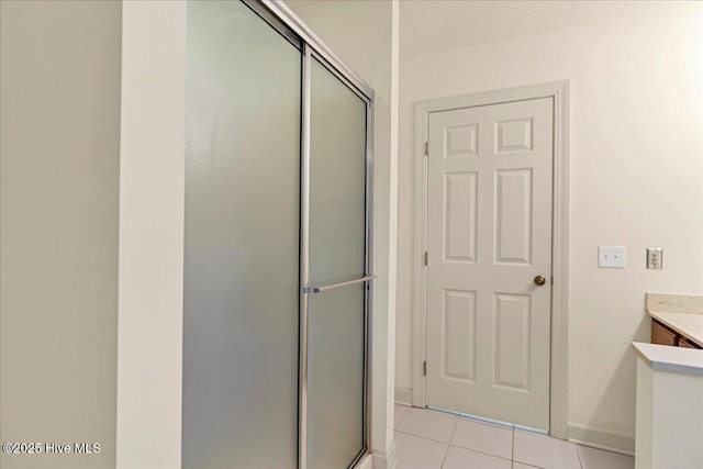 bathroom with vanity, a shower stall, a textured ceiling, baseboards, and tile patterned floors