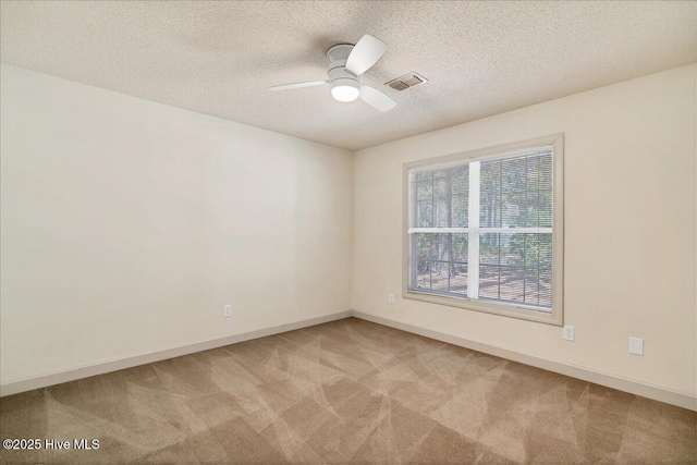 empty room featuring light colored carpet, visible vents, ceiling fan, a textured ceiling, and baseboards