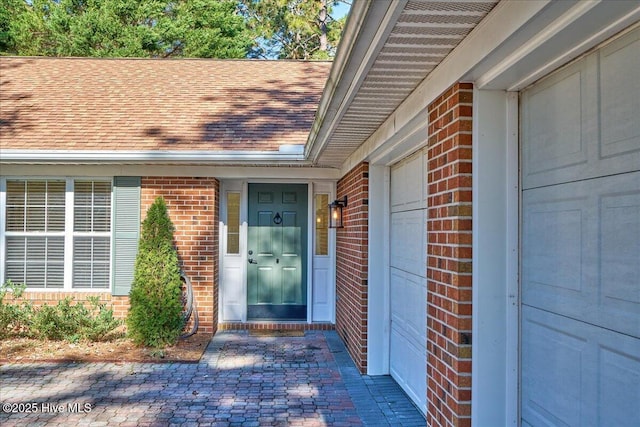 entrance to property featuring brick siding, roof with shingles, and an attached garage