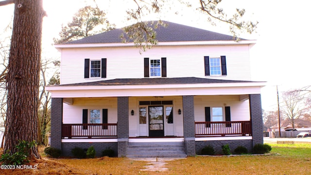 view of front of home with roof with shingles, a front lawn, a porch, and brick siding