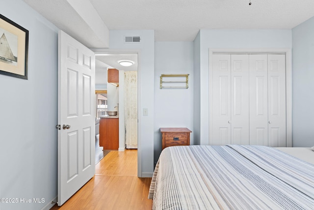 bedroom with light wood-style flooring, a textured ceiling, visible vents, and a closet