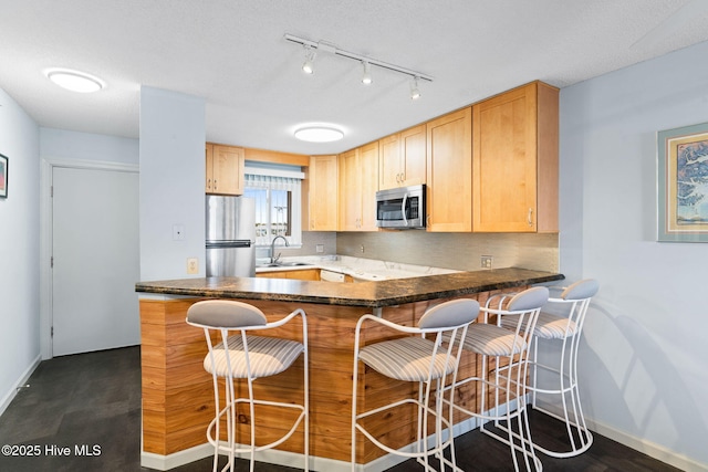 kitchen featuring stainless steel appliances, light brown cabinetry, a peninsula, and a sink