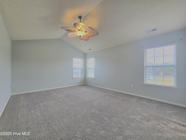 empty room with baseboards, visible vents, vaulted ceiling, a textured ceiling, and carpet flooring