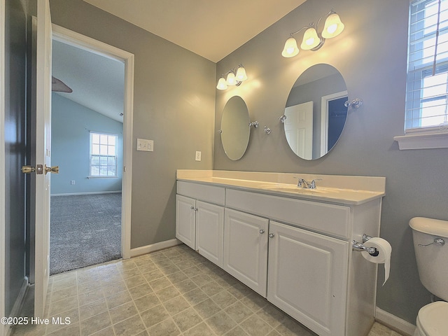 bathroom with toilet, vanity, baseboards, and vaulted ceiling