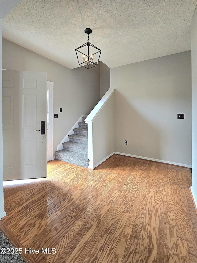 foyer with vaulted ceiling, stairway, an inviting chandelier, and wood finished floors