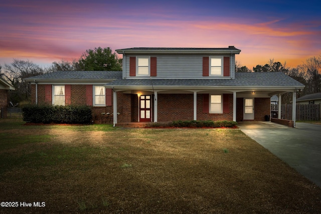 view of front of house with a carport, brick siding, a lawn, and driveway