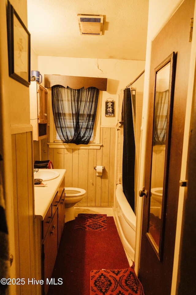 full bathroom featuring toilet, wood walls, vanity, visible vents, and shower / bath combination with curtain