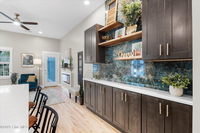 kitchen with light wood finished floors, light countertops, dark brown cabinets, open shelves, and backsplash