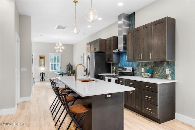 kitchen with a center island with sink, wall chimney exhaust hood, light countertops, appliances with stainless steel finishes, and a kitchen breakfast bar