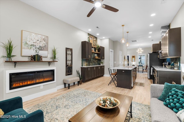 living area with baseboards, light wood finished floors, a glass covered fireplace, and recessed lighting