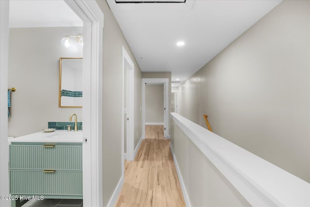 hallway with light wood-style floors, baseboards, a sink, and an upstairs landing