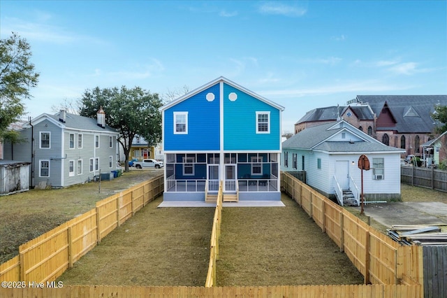 rear view of property featuring entry steps, a fenced backyard, a sunroom, a lawn, and a residential view