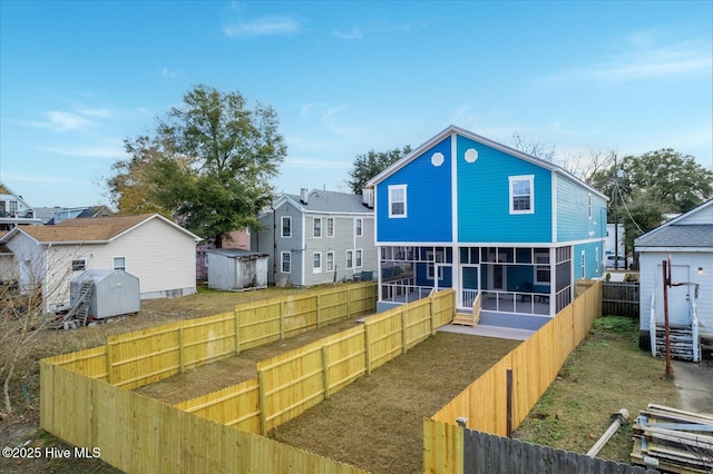 rear view of property featuring a storage shed, a residential view, a fenced backyard, and a sunroom