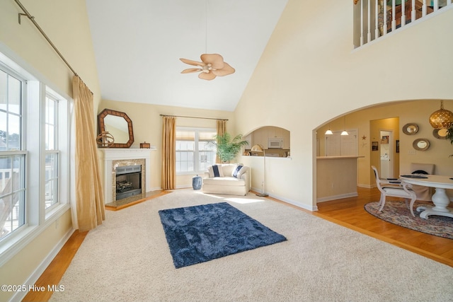 living room featuring wood finished floors, a fireplace, arched walkways, ceiling fan, and a towering ceiling