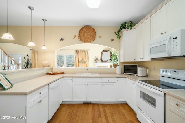 kitchen with light countertops, light wood-style floors, hanging light fixtures, white appliances, and a sink