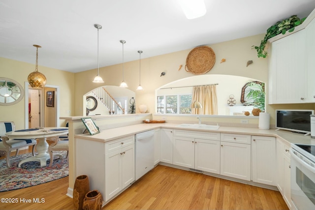 kitchen featuring decorative light fixtures, light countertops, light wood-type flooring, white appliances, and a sink