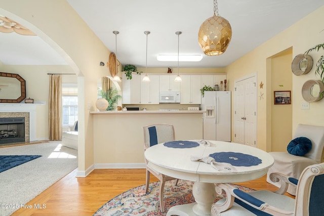 dining area with arched walkways, a tiled fireplace, light wood-type flooring, and baseboards