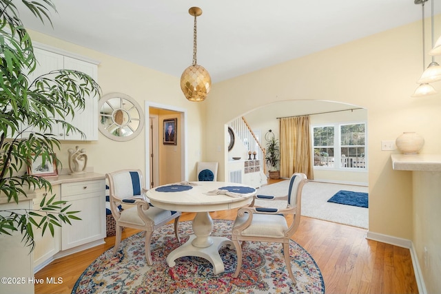 dining room featuring stairs, light wood-style floors, arched walkways, and baseboards