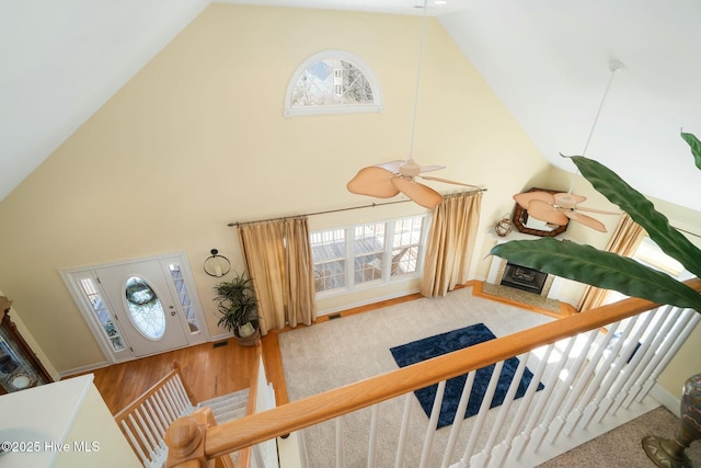 interior space with a ceiling fan, wood finished floors, a fireplace with raised hearth, and high vaulted ceiling