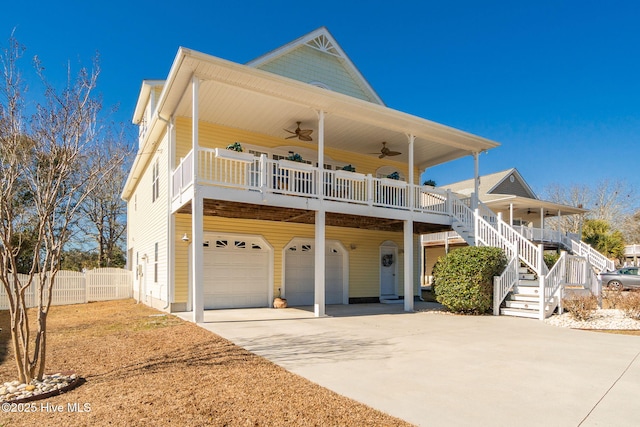 raised beach house featuring ceiling fan, fence, concrete driveway, stairs, and an attached garage