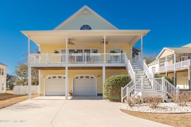 coastal home with ceiling fan, stairway, concrete driveway, covered porch, and an attached garage