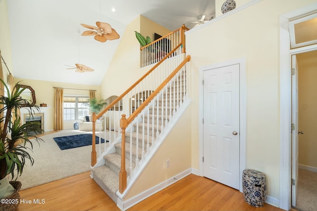 stairs featuring baseboards, high vaulted ceiling, a ceiling fan, and wood finished floors