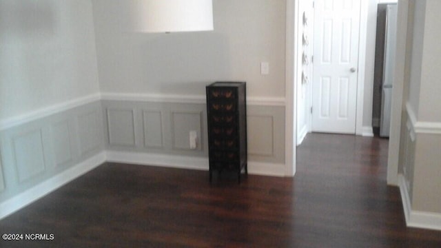 empty room featuring dark wood-style floors, a decorative wall, and wainscoting