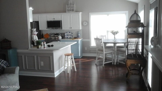 kitchen with a breakfast bar, stainless steel appliances, light countertops, dark wood-type flooring, and white cabinets