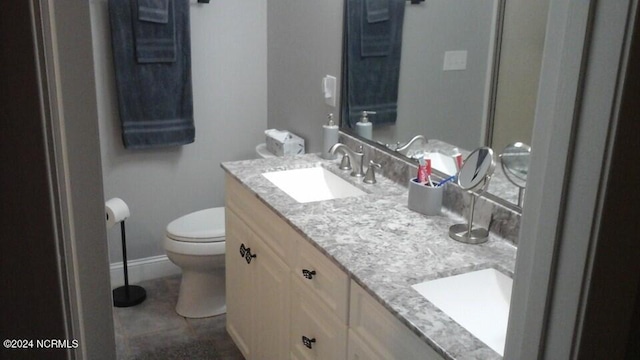 bathroom featuring double vanity, baseboards, toilet, and a sink