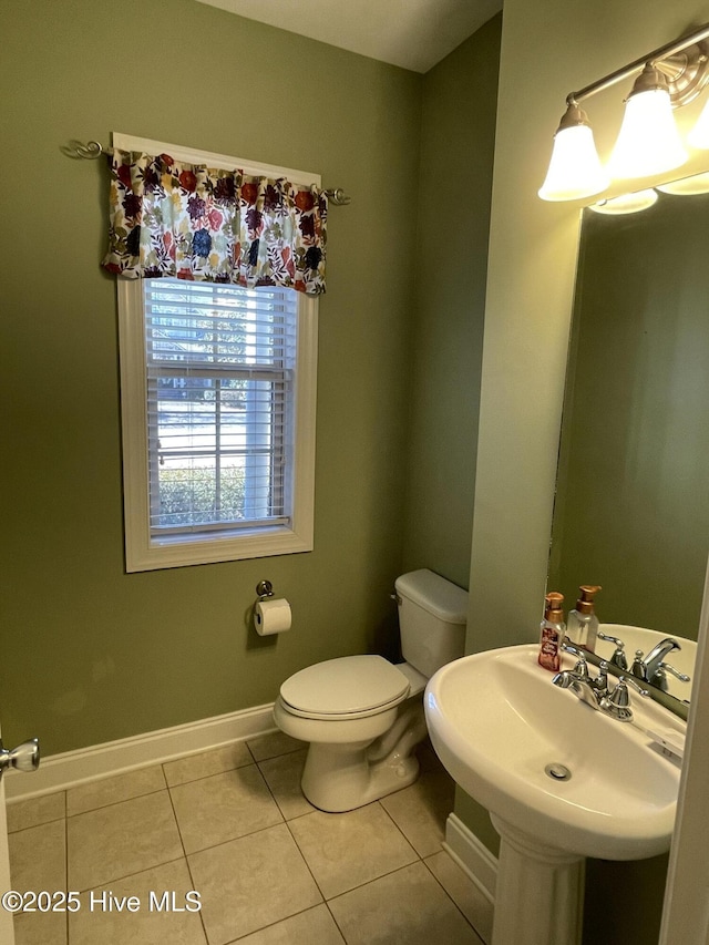 half bath with toilet, tile patterned flooring, baseboards, and a sink