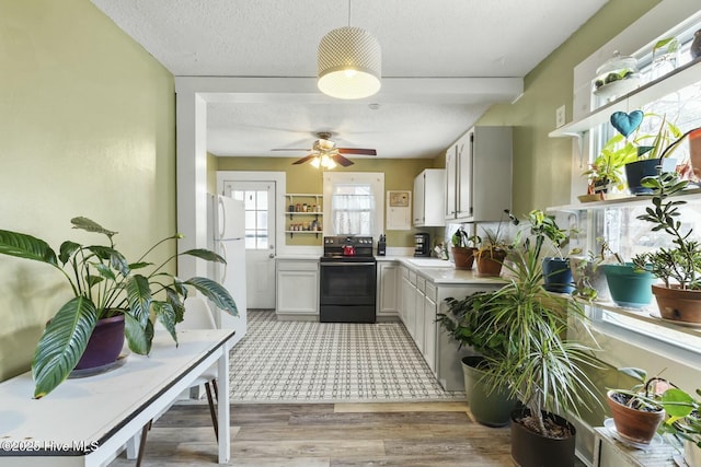 kitchen featuring a textured ceiling, a sink, white cabinets, black electric range, and light countertops